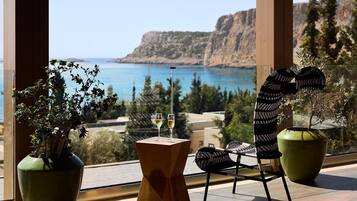 Un balcón con vista al mar, una mesa con dos copas de vino y dos plantas en macetas.
