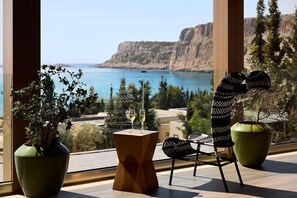 Un balcone con vista sul mare, un tavolo con due bicchieri di vino e due vasi con piante.