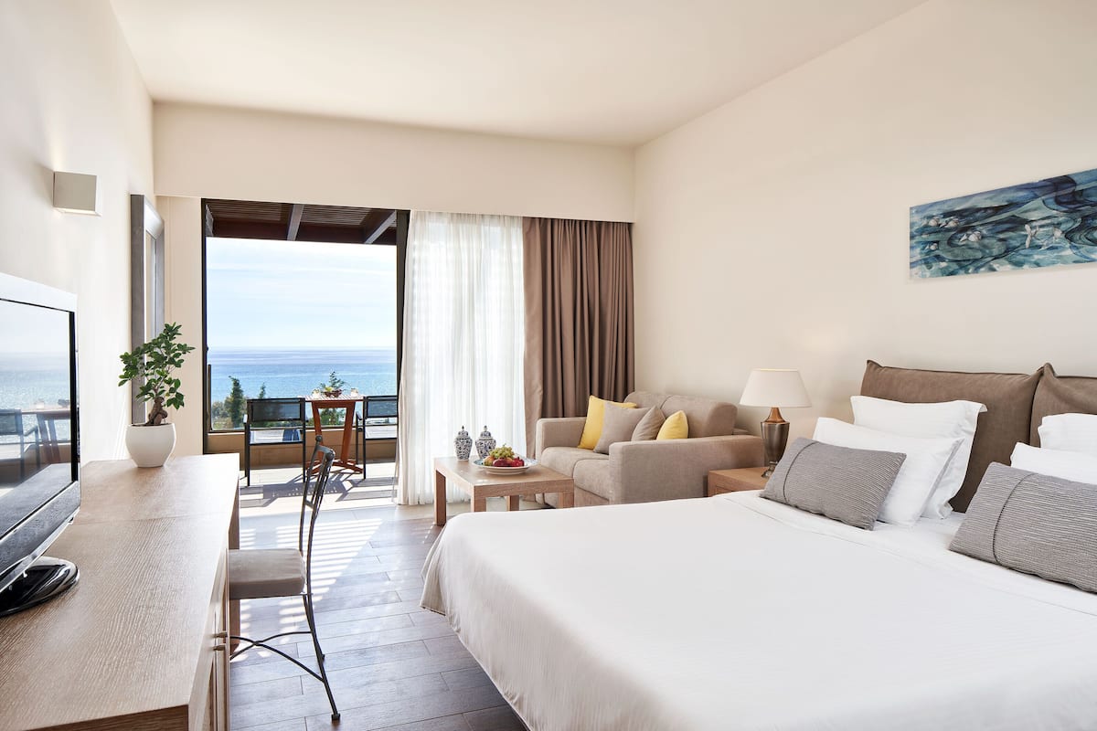 Une chambre d’hôtel avec un lit, un canapé, une télévision, une table à manger et une vue sur la mer.