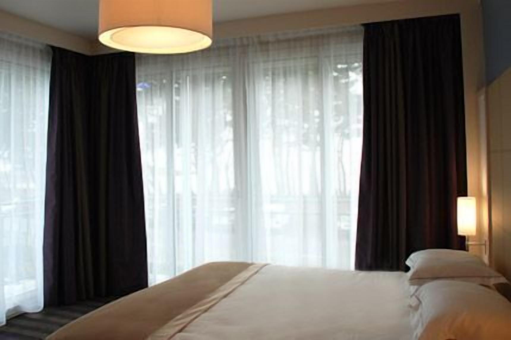 Een hotelkamer met een groot bed, een bedlampje en dunne gordijnen.
