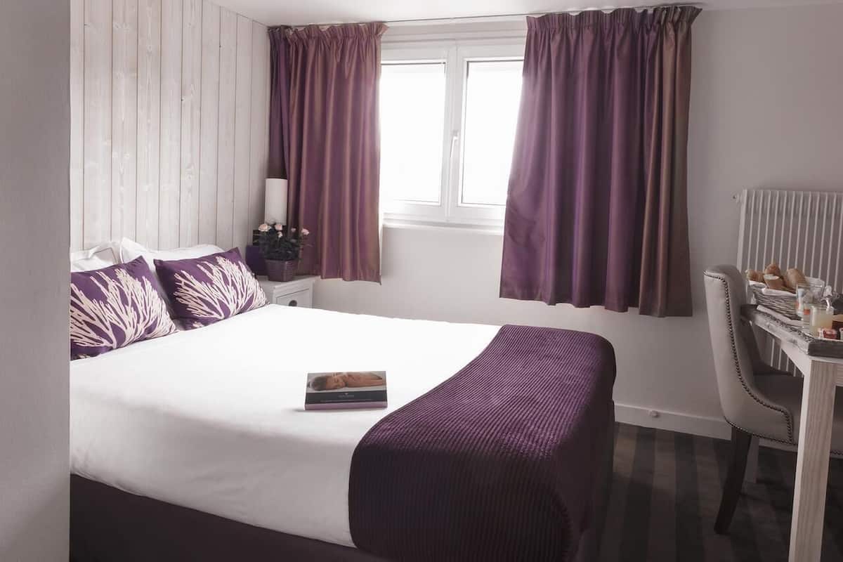 Une chambre d’hôtel bien aménagée, avec un grand lit, une table de chevet avec une lampe, une chaise et une fenêtre avec des rideaux.