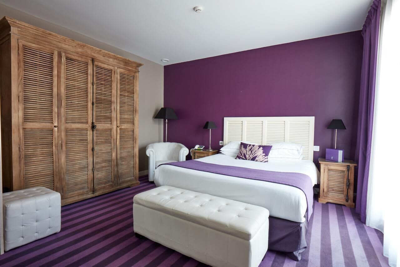 A bedroom with a large bed, a wardrobe, a chair, a bedside table, and a bench.