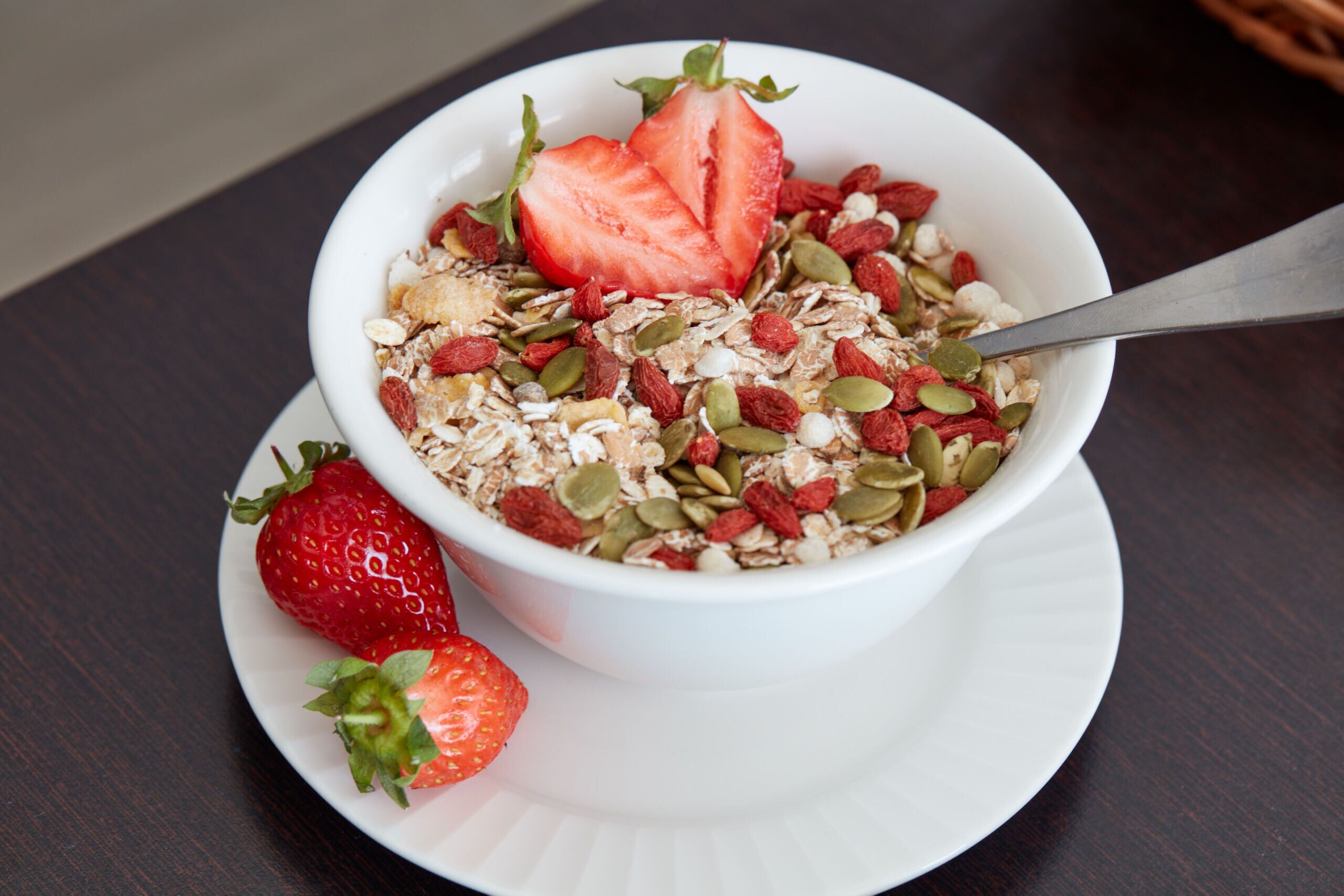 Un tazón de cereal con fresas y semillas sobre un plato blanco.