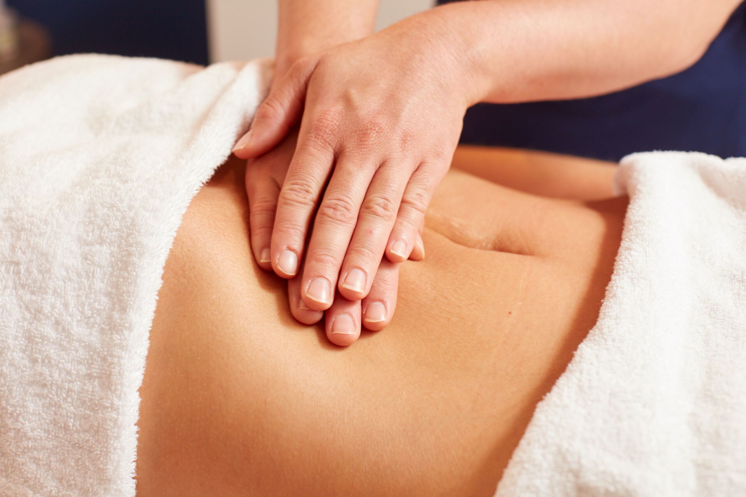 A person receiving a massage with hands on their back, covered by a white towel.