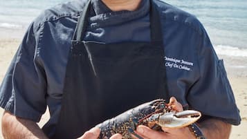 A person holding a lobster on a beach with houses in the background.