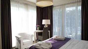 A hotel room with a bed, a chair, a table with a lamp, and a view of the city.