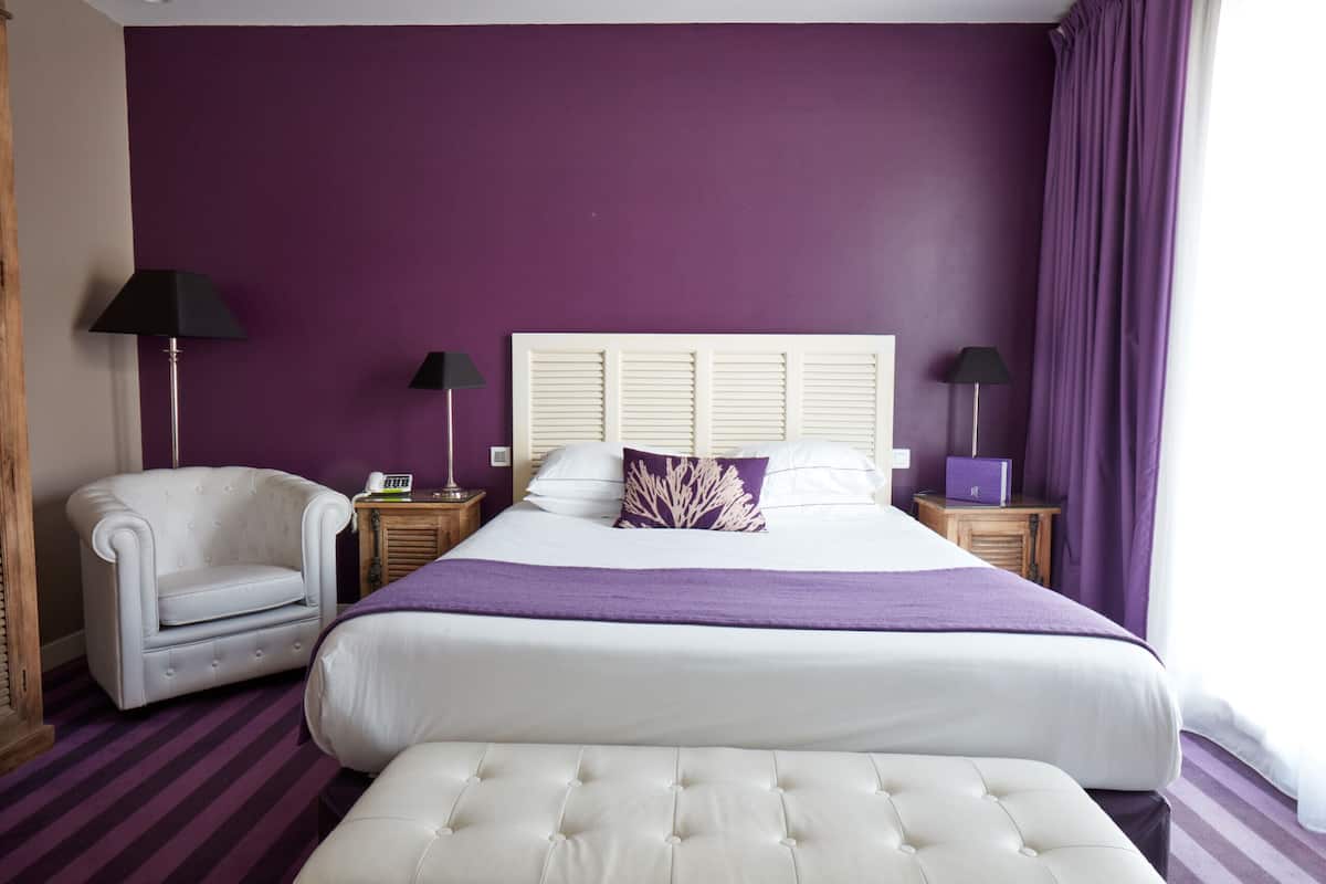 Une chambre à coucher avec un grand lit, une chaise, deux tables de chevet et des rideaux violets.