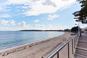 Une plage avec une promenade en bois, un rivage sablonneux et une mer calme.