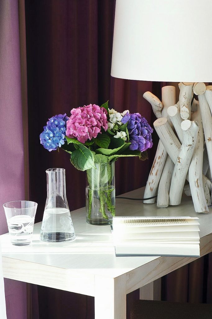 A desk with a vase of flowers, a glass flask, a notebook, and a lamp.