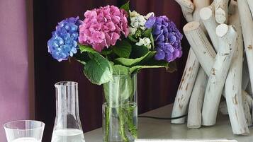 A desk with a vase of flowers, a glass flask, a notebook, and a lamp.