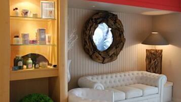 Ein Zimmer mit einem weißen Sofa, einem Holzboden mit Pflegeprodukten, einem runden Spiegel und einer Lampe.