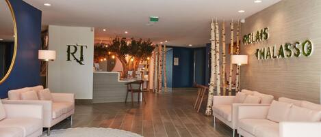 Un vestíbulo de hotel con un mostrador de recepción, dos sofás, un espejo grande y una pared con el nombre del hotel.