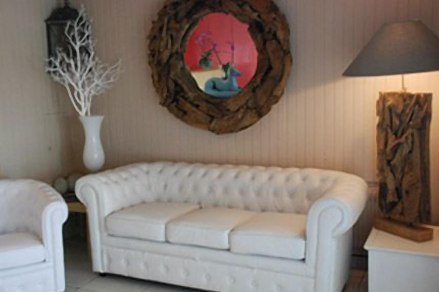 A white upholstered sofa in a room with a decorative wooden frame on the wall, a white vase with branches, and a lamp on a side table.
