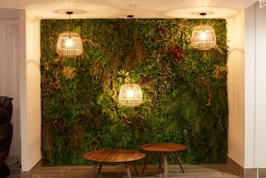 Une pièce avec un mur vert recouvert de plantes et deux tables en bois.