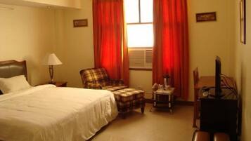 A hotel room with a bed, a chair, a small table, a lamp, and a television.