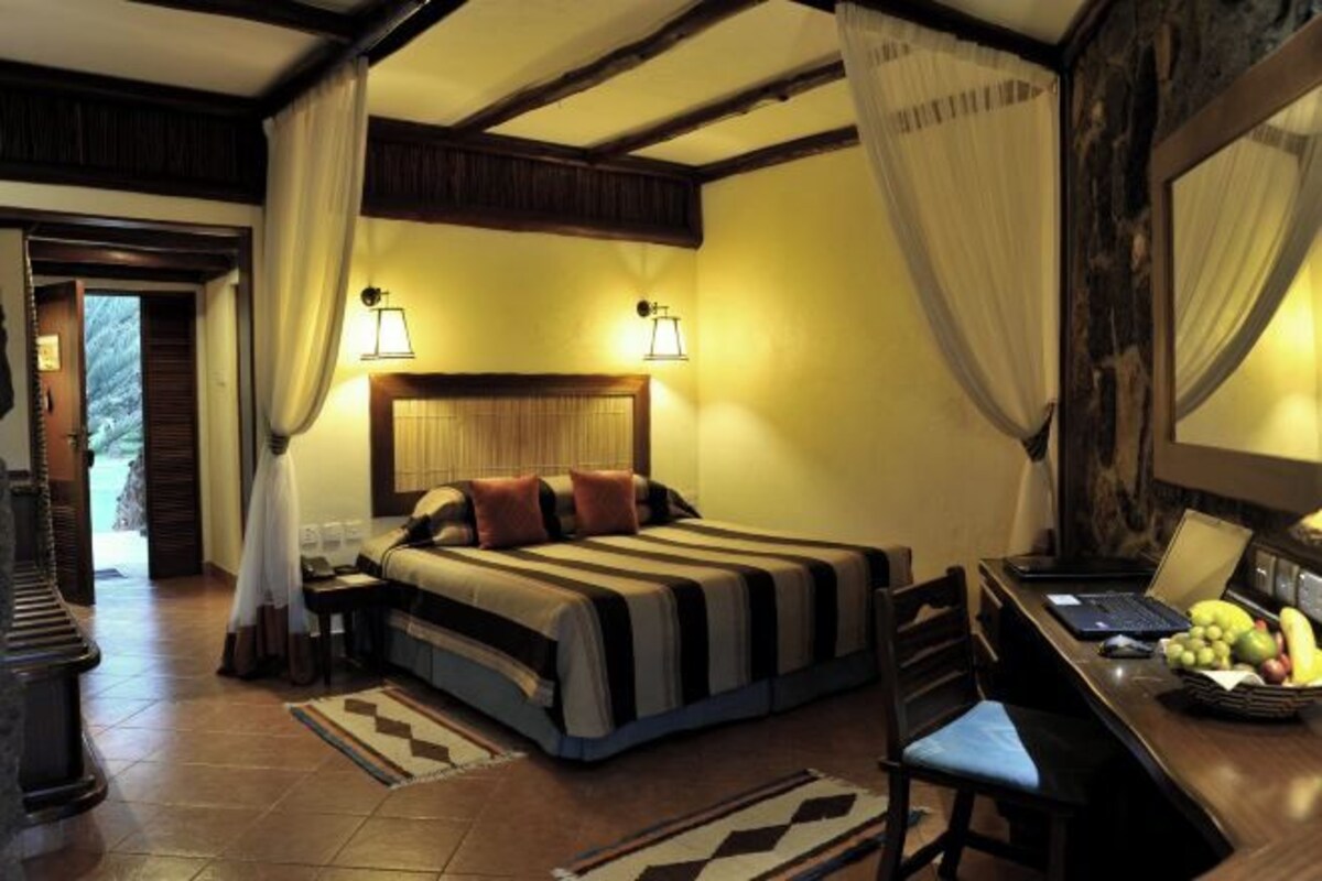 Un dormitorio con cama, mesita de noche, lámpara y un escritorio con silla.