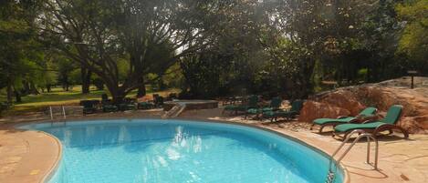 A swimming pool with a curved edge, surrounded by lounge chairs and a stone deck.