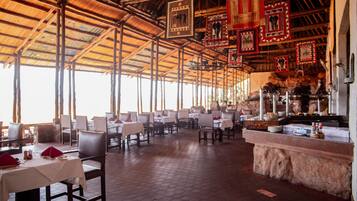 Un restaurante con techos altos, azulejos decorativos en el techo y una zona de bufé con mostrador de piedra. Las mesas están dispuestas con manteles blancos y servilletas rojas.