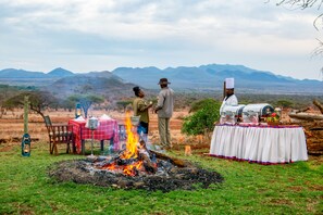 A campsite with a fire, tables, chairs, and a portable grill. - Kilaguni Serena Safari Lodge (Tsavo)