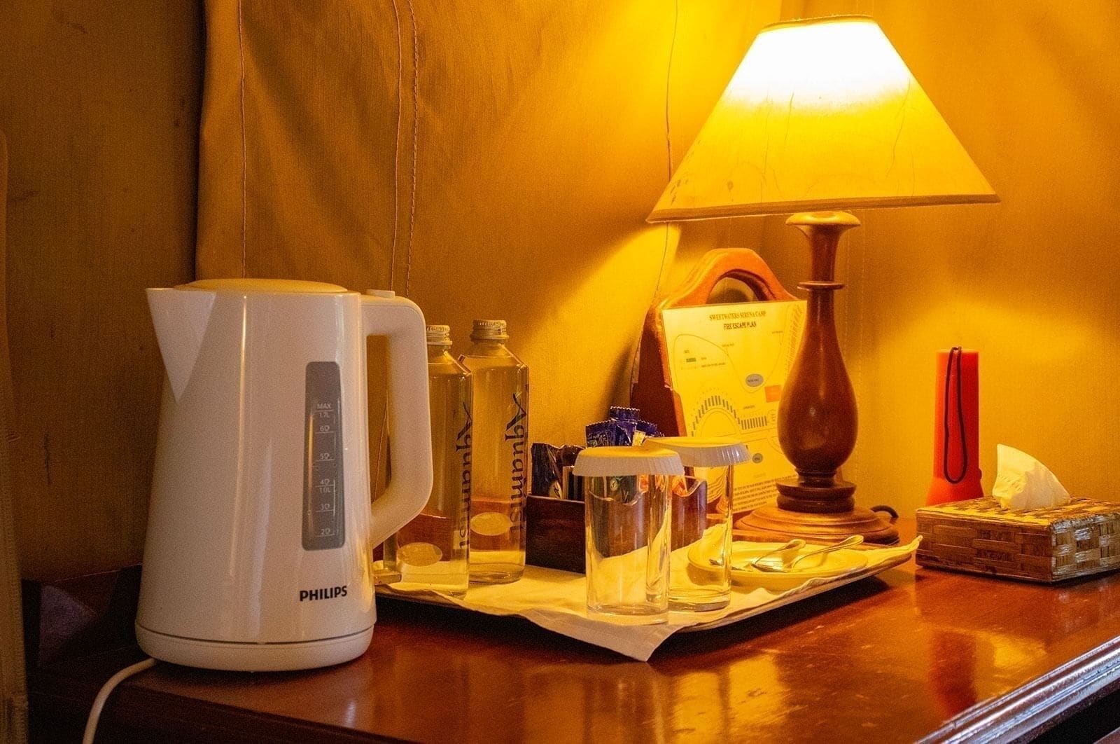 A hotel room with a white Philips coffee maker, a table lamp, and various toiletries on a wooden table.