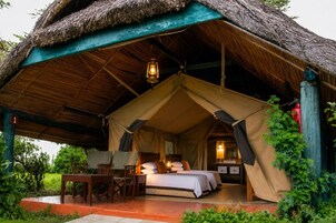 A tented accommodation with a bed, bedside tables, and a hanging lantern.