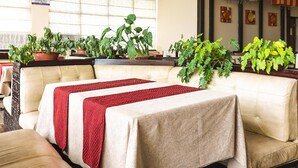 A seating area with cushioned sofas and tables, each with a tablecloth and a red decorative runner. - Hotel Asia Vaishno Devi (Reasi)