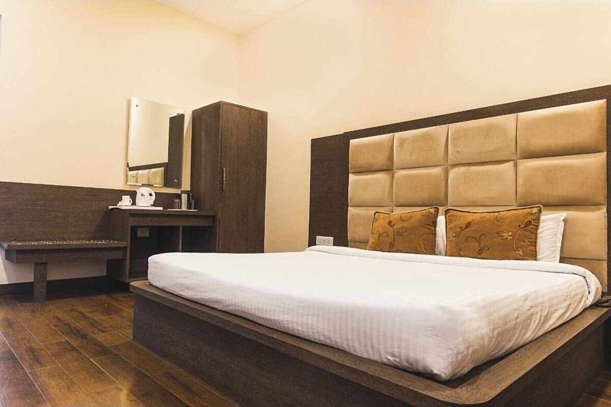 A hotel room with a large bed, a wooden bench, a wardrobe, and a mirror.
