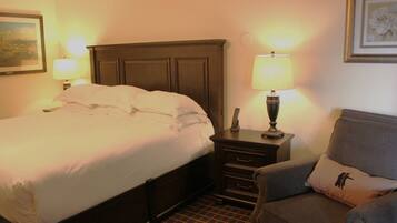 A hotel room with a large bed, a nightstand with a lamp, a chair, and a framed picture on the wall.
