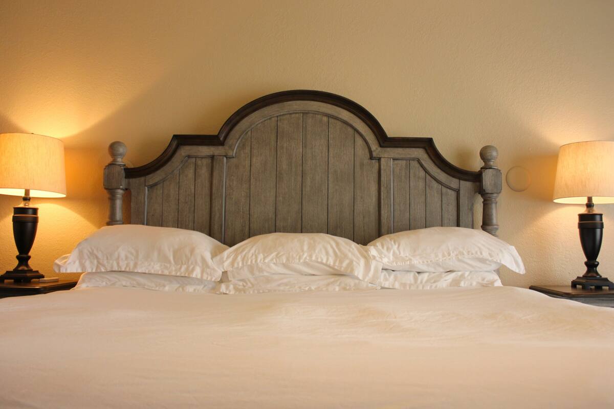 A bed with a wooden headboard, two bedside lamps, and white bedding.