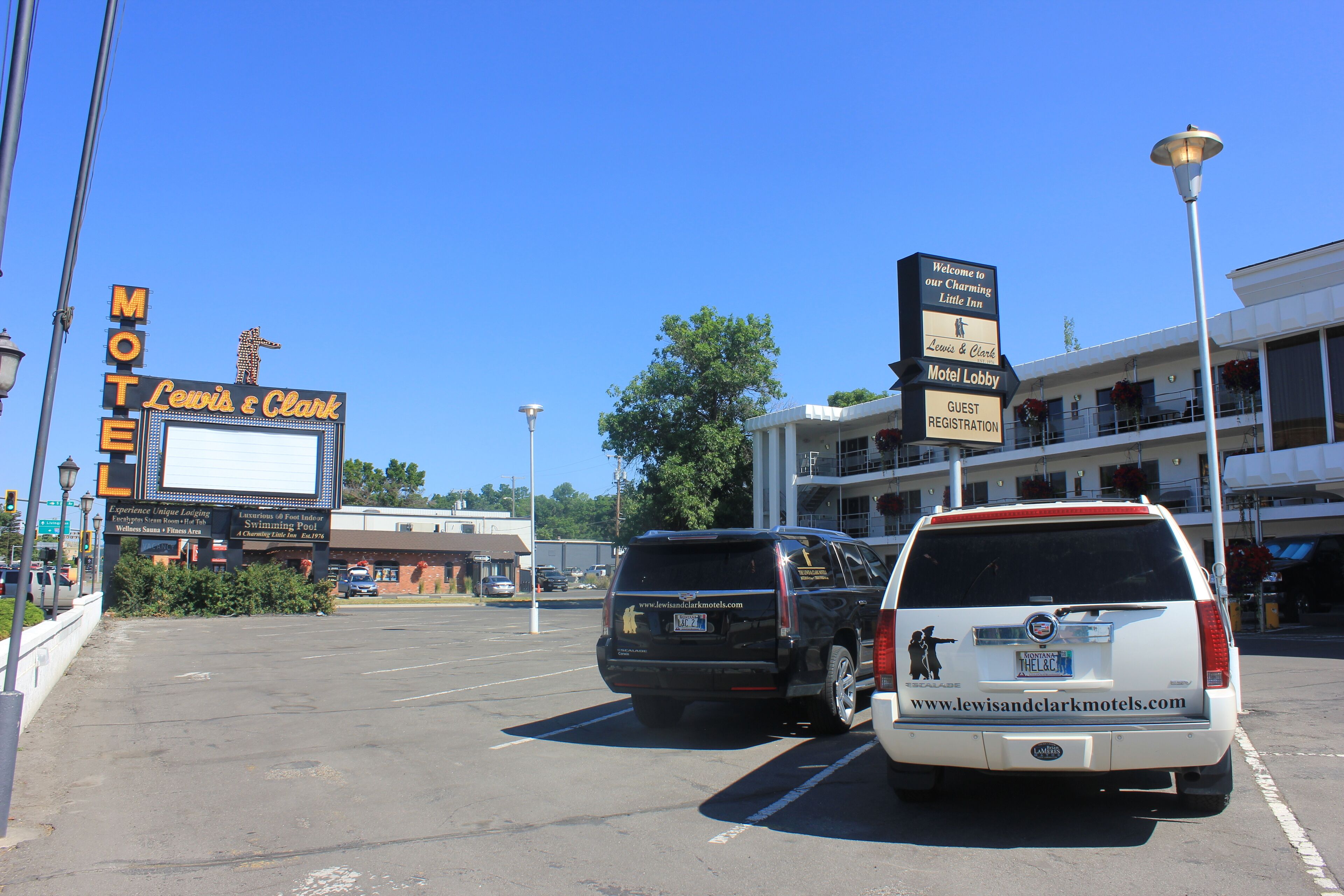 Ein Motel mit einer großen Schautafel, einer Rezeption und einem Parkplatz mit Fahrzeugen.