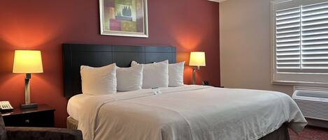 A hotel room with a large bed, two bedside lamps, a painting on the wall, and a window with blinds.