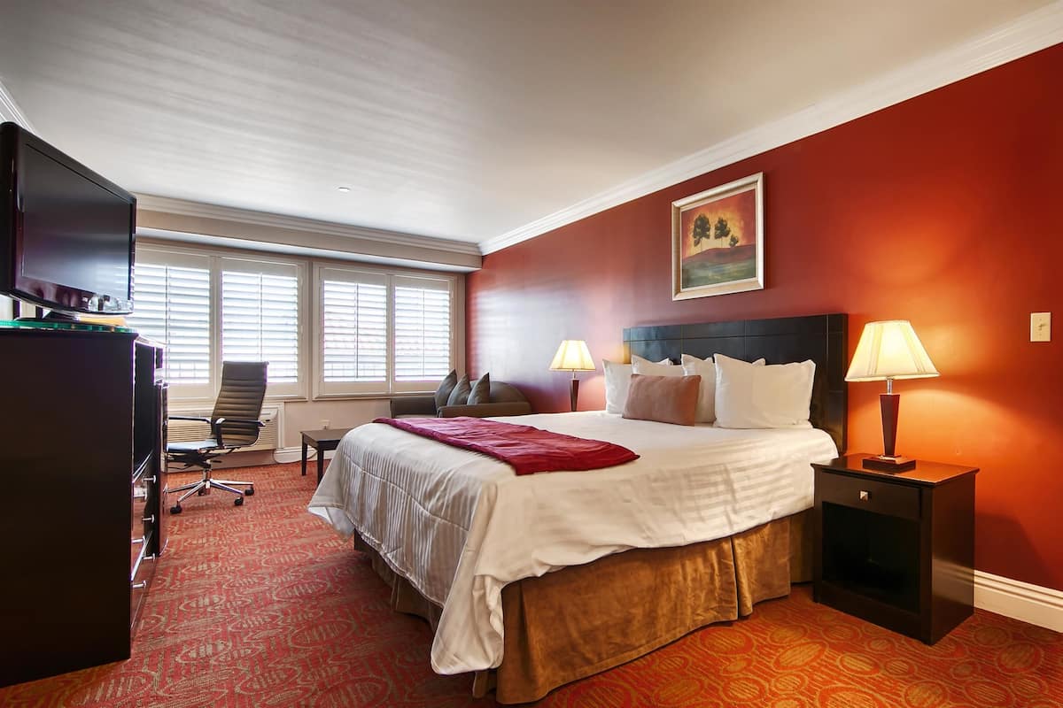 A hotel room with a large bed, two bedside lamps, a desk with a computer, and a chair.