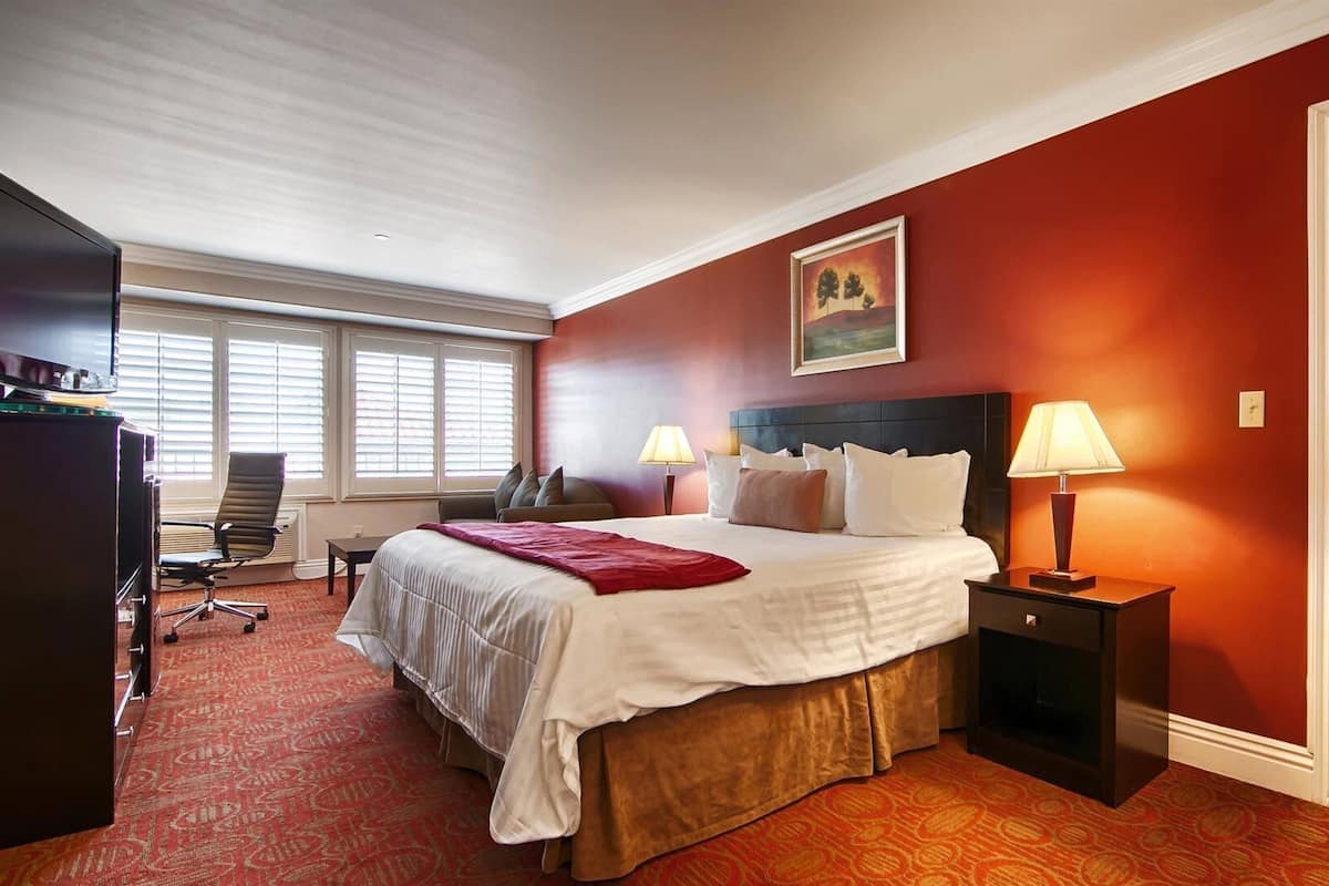 Habitación de hotel con una cama grande, dos lámparas de noche, un escritorio con computadora y una ventana con persianas.
