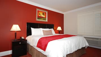 A hotel room with a large bed, two bedside lamps, a painting on the wall, a telephone, and a window with blinds.