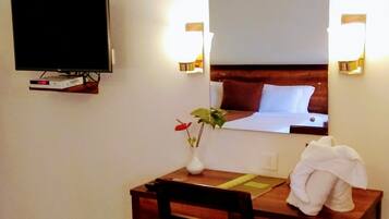 Habitación de hotel con un escritorio de madera, una silla, un televisor montado en la pared, un espejo y una toalla blanca sobre la silla.