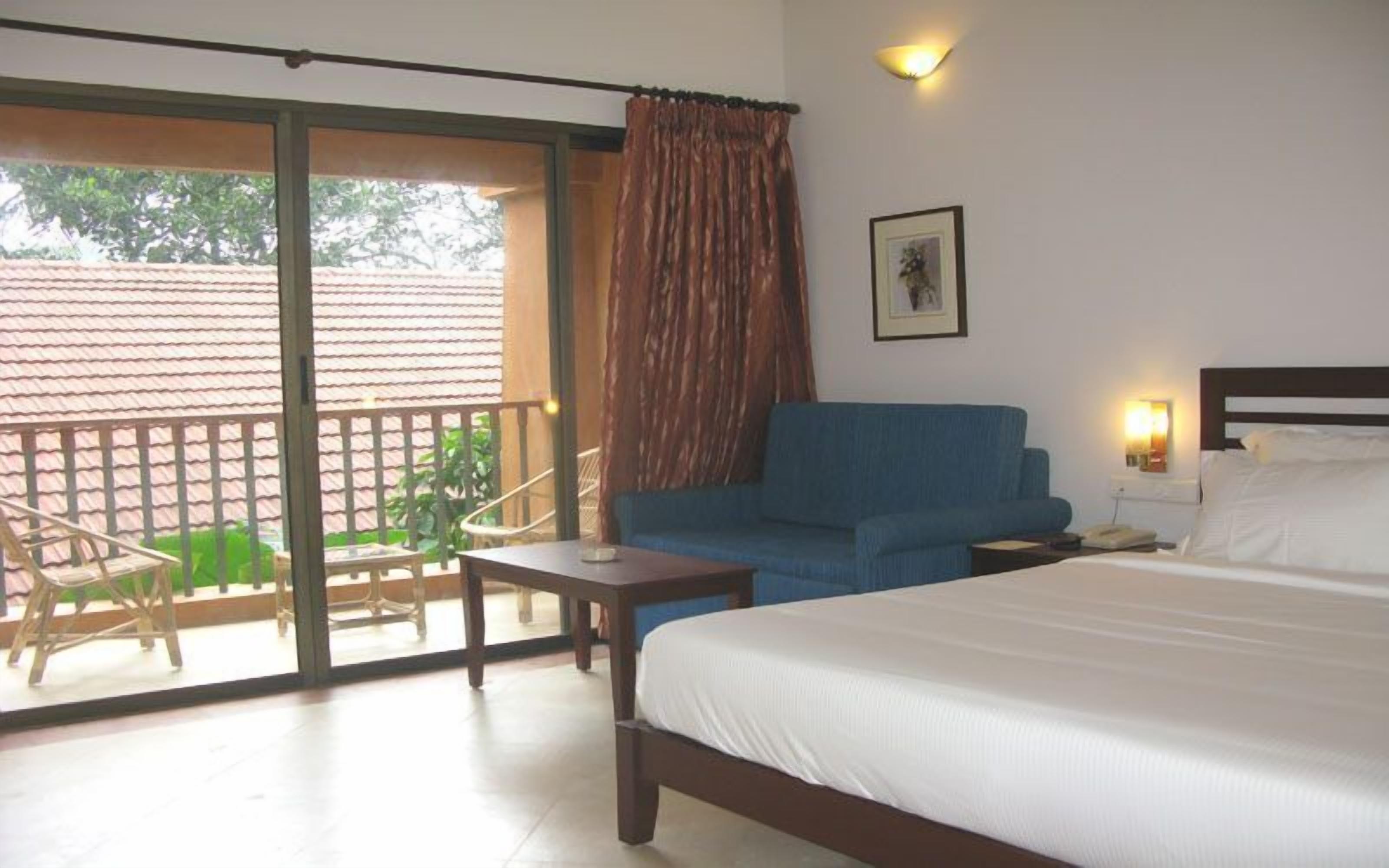 A hotel room with a bed, a sofa, a table, a chair, and a balcony with a view of the outside.