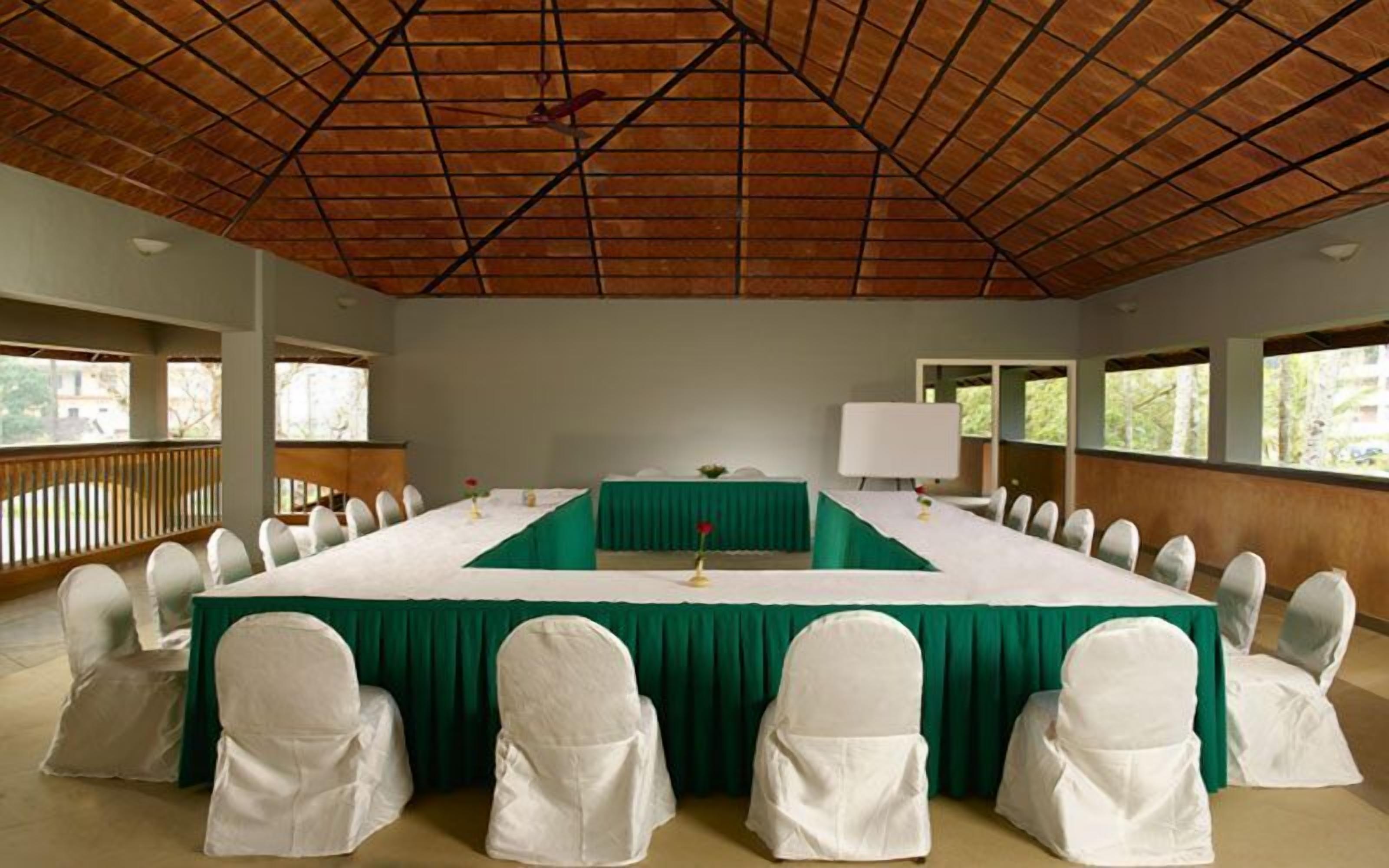 A conference room with a long table, white chairs, and a green tablecloth.