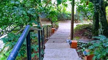 A concrete pathway leading through a garden with potted plants and a metal railing on one side.