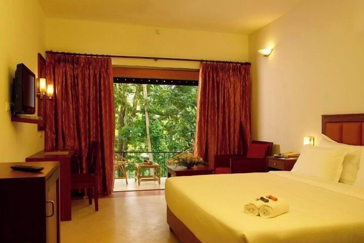 A hotel room with a bed, a desk, a television, and a balcony with curtains.