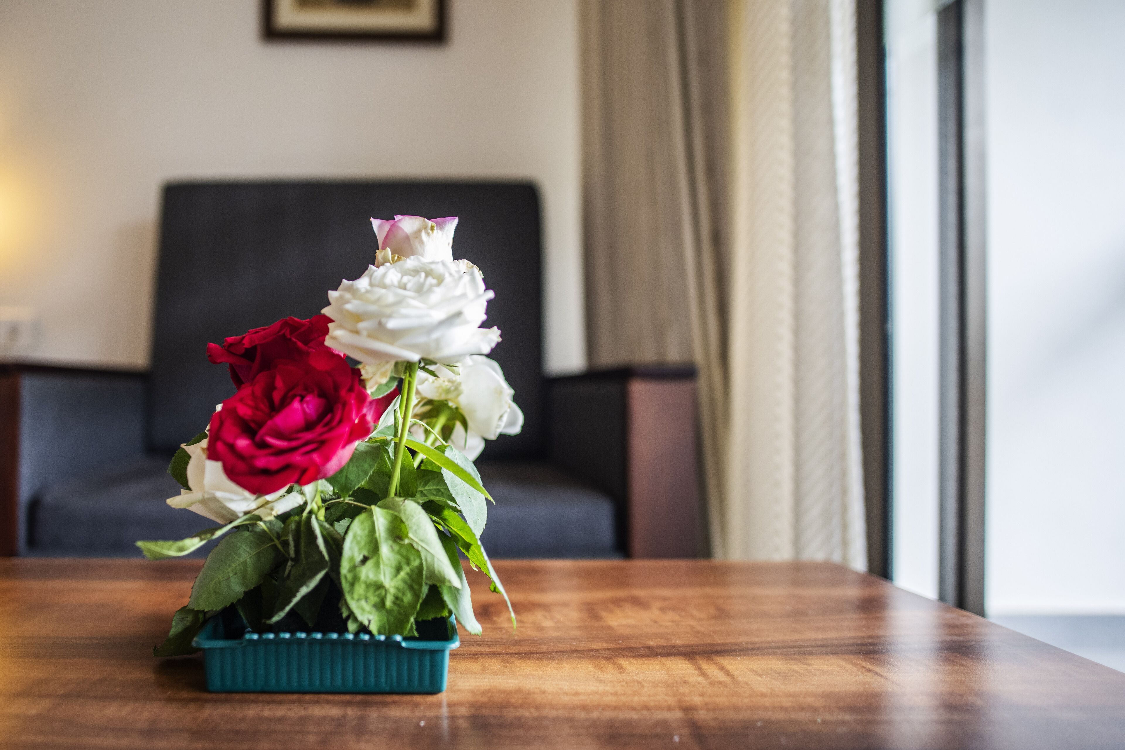 A wooden table with a teal vase containing red and white roses.