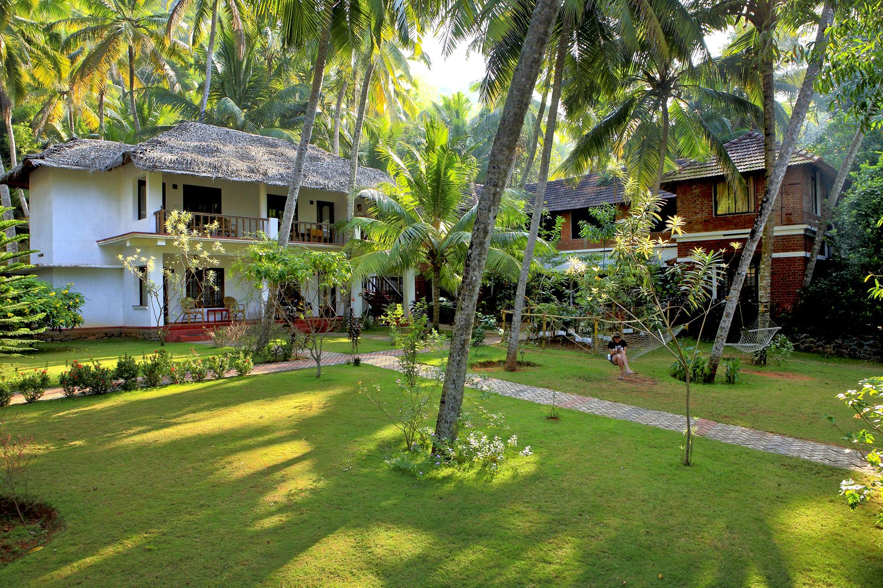 A bungalow with a thatched roof, surrounded by lush greenery and palm trees.