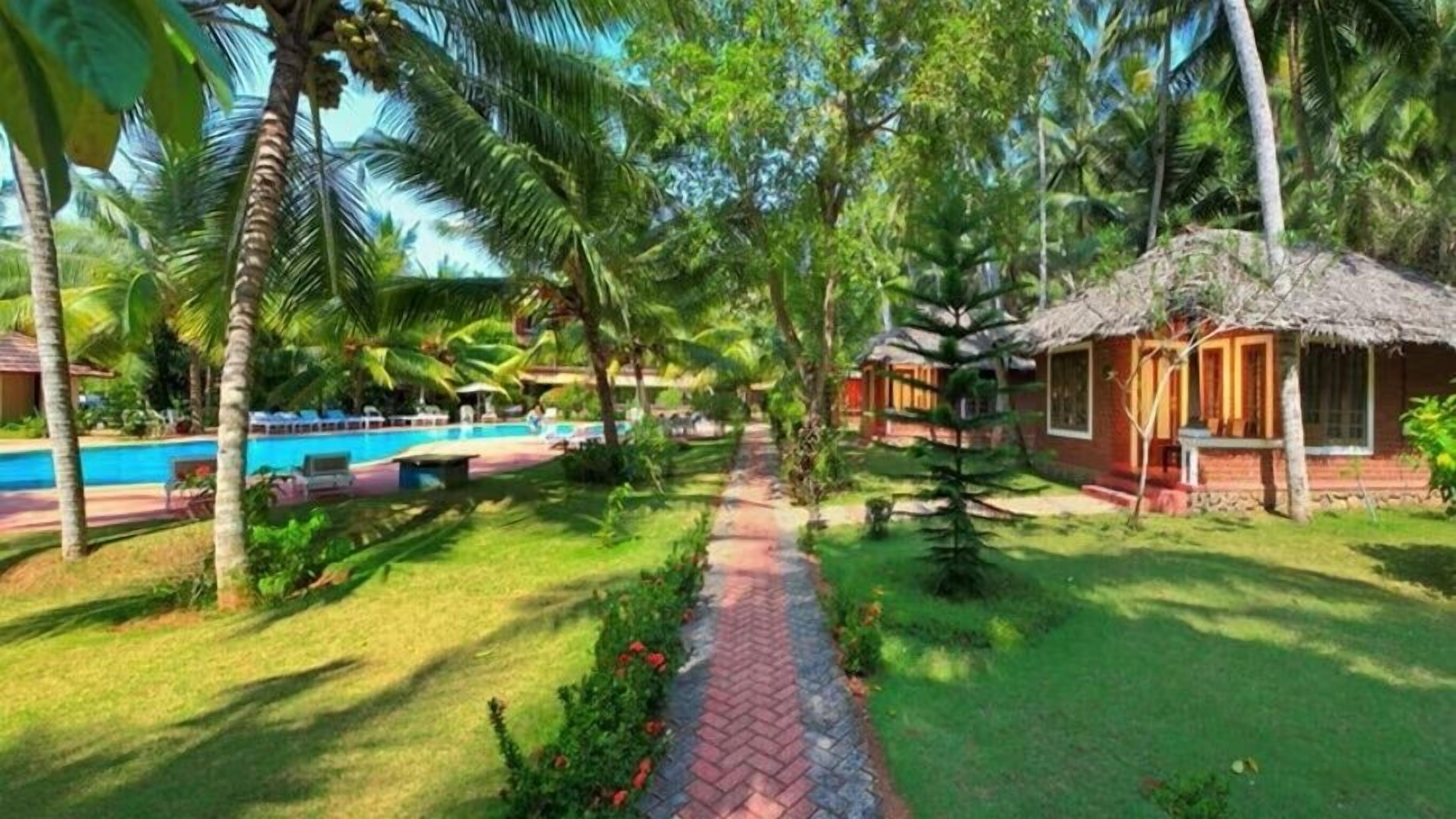 Zona de piscina con sendero de ladrillo, palmeras y cabañas de techo de paja.