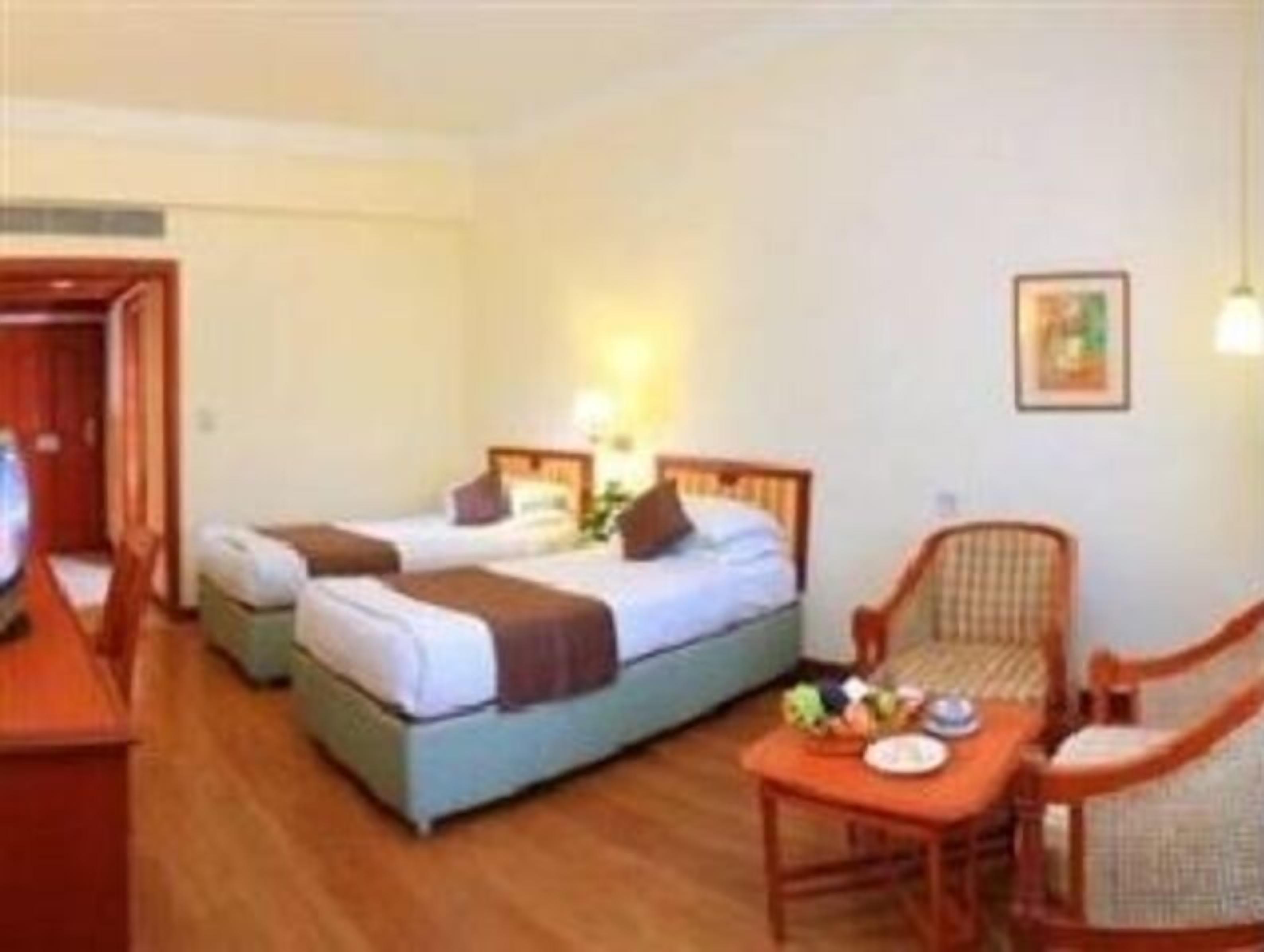 Habitación de hotel con dos camas, un escritorio, una silla y una mesita con un plato y un bol.