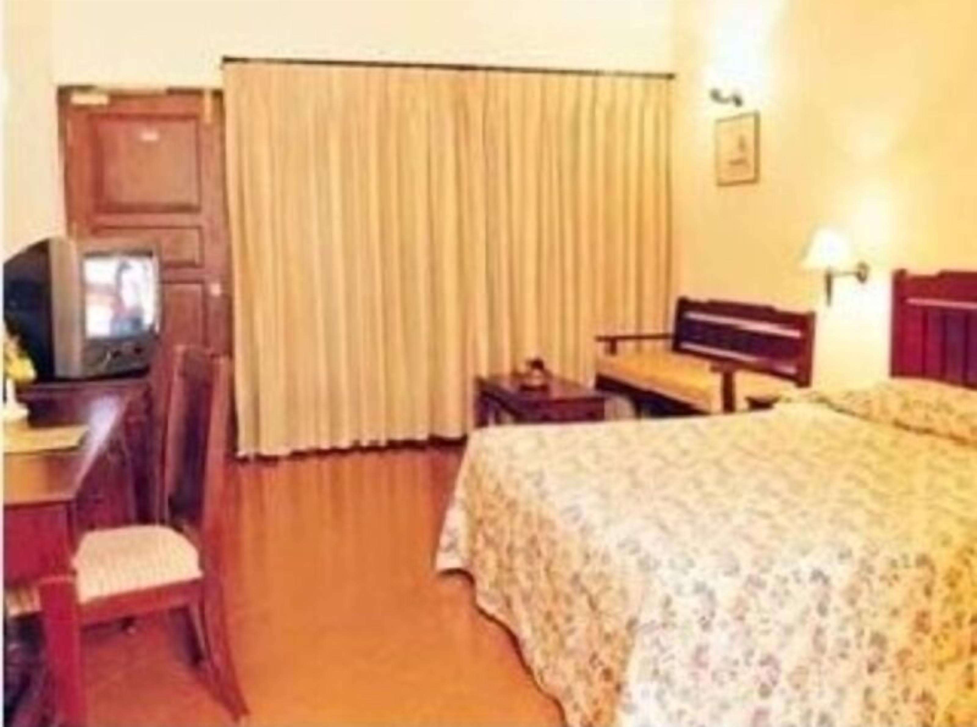 Una habitación de hotel con una cama, un escritorio con silla, televisión y ventana con cortinas.