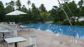 A swimming pool with lounge chairs and umbrellas, surrounded by palm trees.