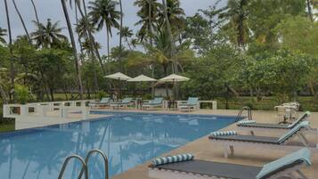 Una piscina con sillones de descanso y sombrillas, rodeada de palmeras.
