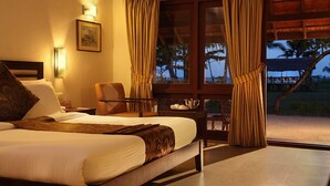 Una habitación de hotel con cama, una silla, una mesita de noche y un ventanal con cortinas.