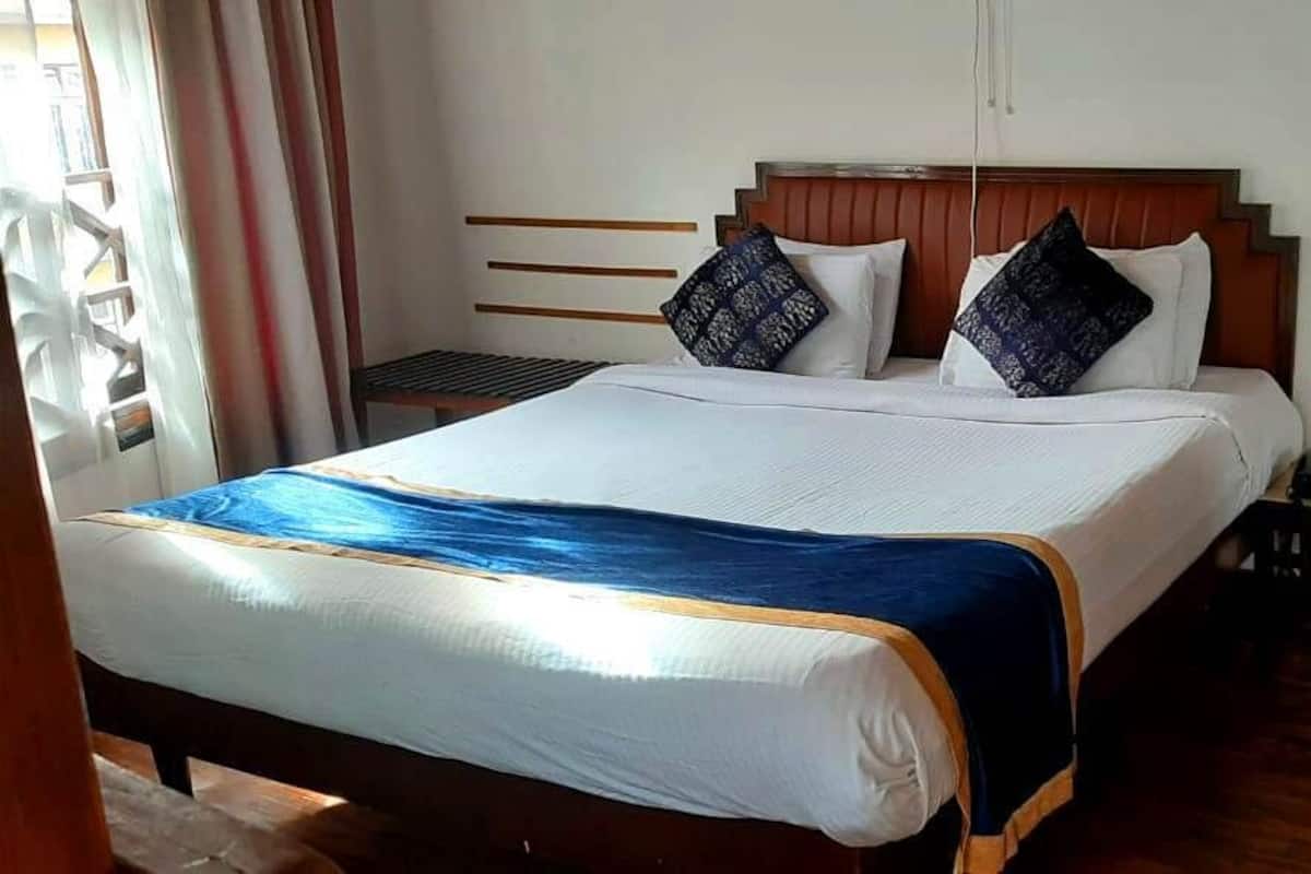 Ein ordentlich bezogenes Bett mit einer blau-weißen Tagesdecke, zwei Kissen und einem Holzkopfteil.