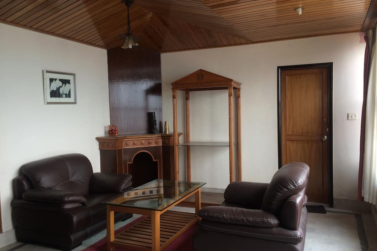 Ein Wohnzimmer mit Holzboden, einem Glastisch, zwei Ledersofas, einem Holzschrank und einer Tür.