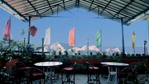 Un patio al aire libre con mesas y sillas redondas, rodeado de plantas en macetas y banderas.